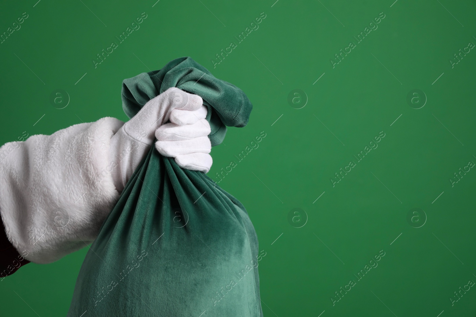 Photo of Santa Claus with bag of Christmas gifts on green background, closeup. Space for text