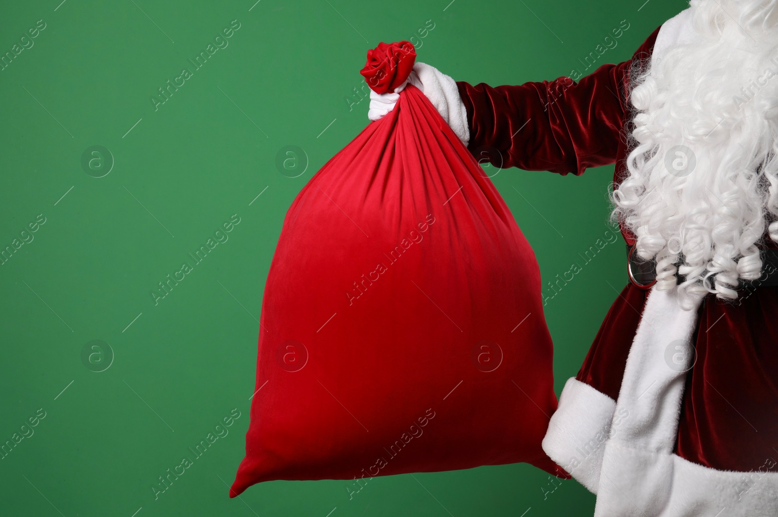 Photo of Santa Claus with red bag of Christmas gifts on green background, closeup