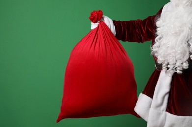 Photo of Santa Claus with red bag of Christmas gifts on green background, closeup