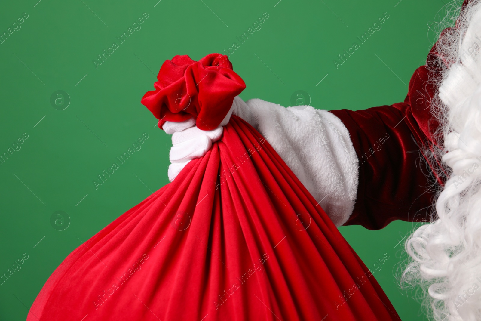 Photo of Santa Claus with red bag of Christmas gifts on green background, closeup