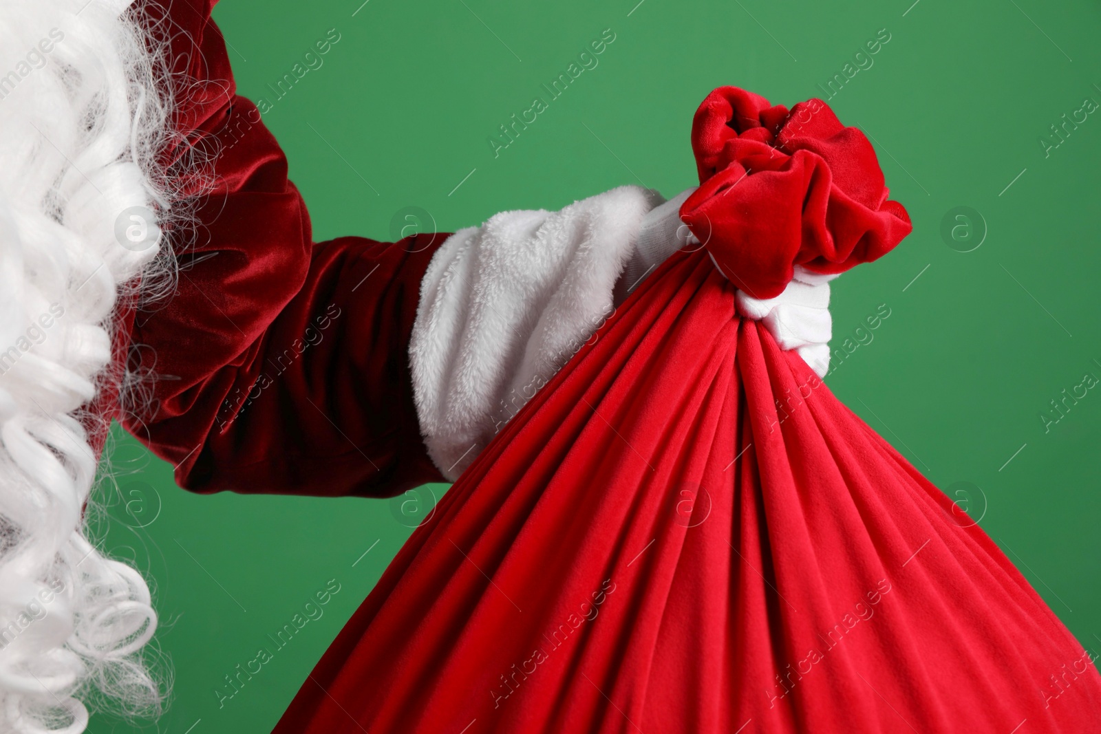 Photo of Santa Claus with red bag of Christmas gifts on green background, closeup