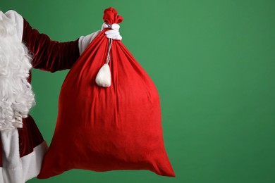 Photo of Santa Claus with red bag of Christmas gifts on green background, closeup. Space for text