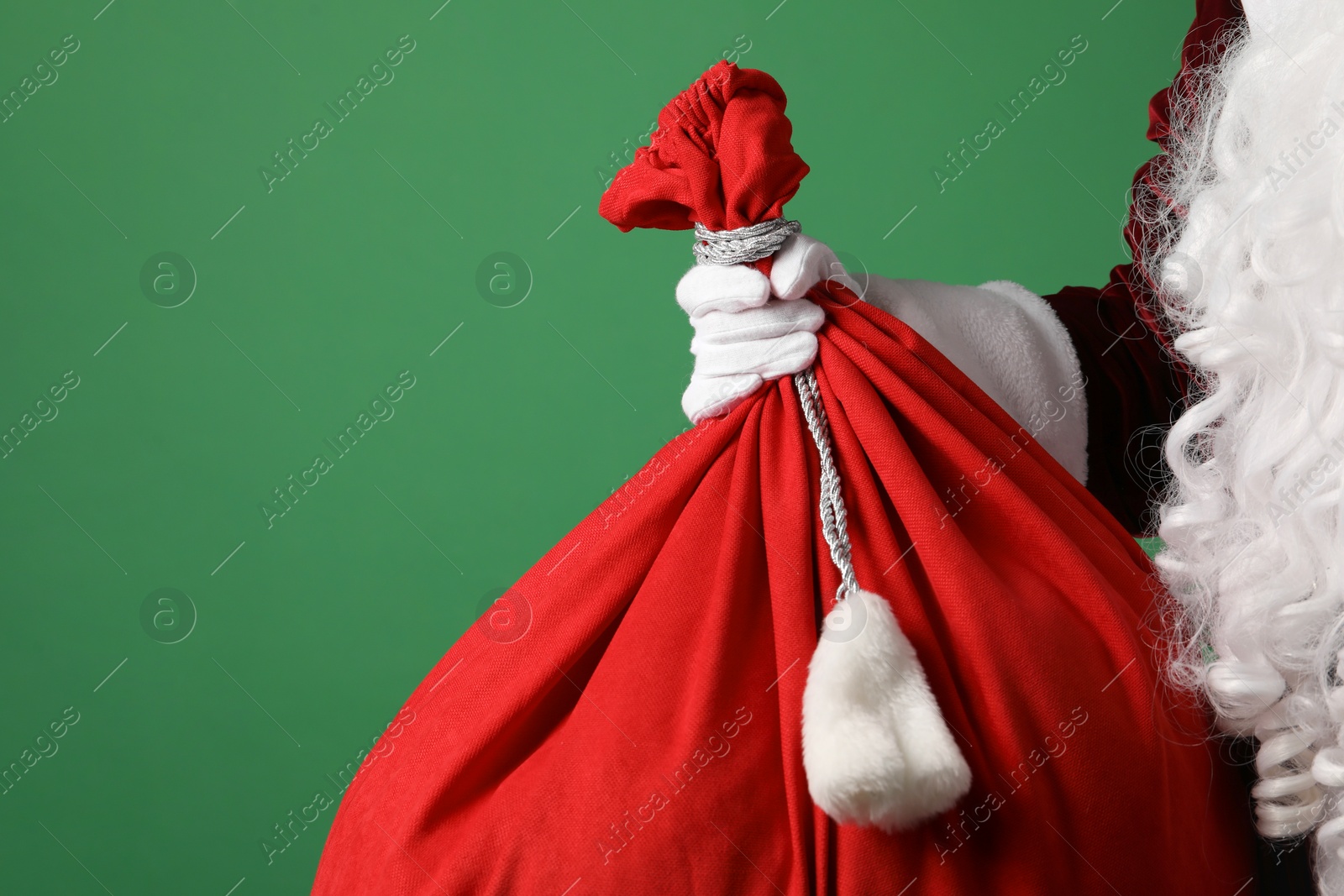 Photo of Santa Claus with red bag of Christmas gifts on green background, closeup