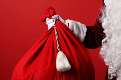 Photo of Santa Claus with bag of Christmas gifts on red background, closeup