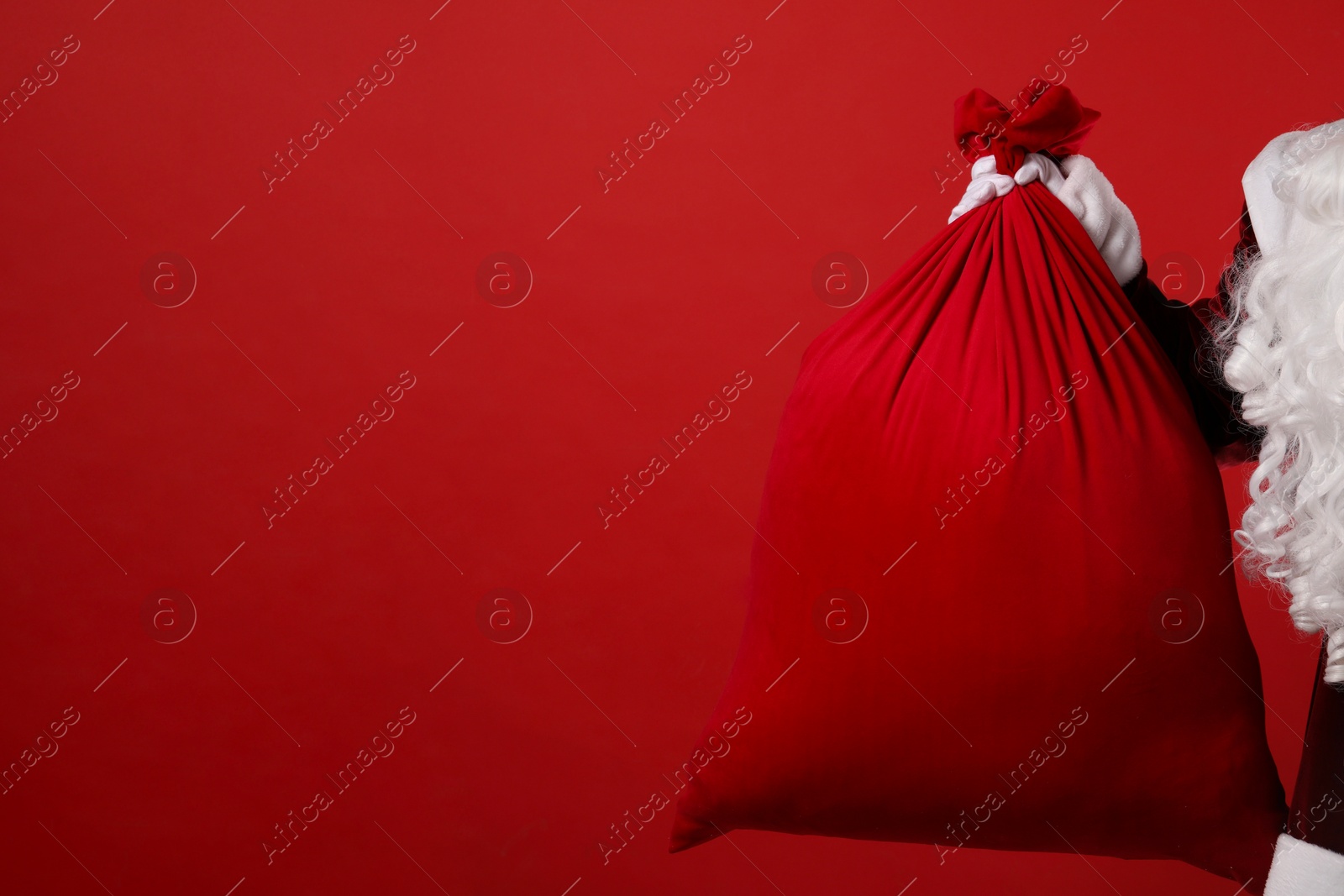 Photo of Santa Claus with bag of Christmas gifts on red background, closeup. Space for text