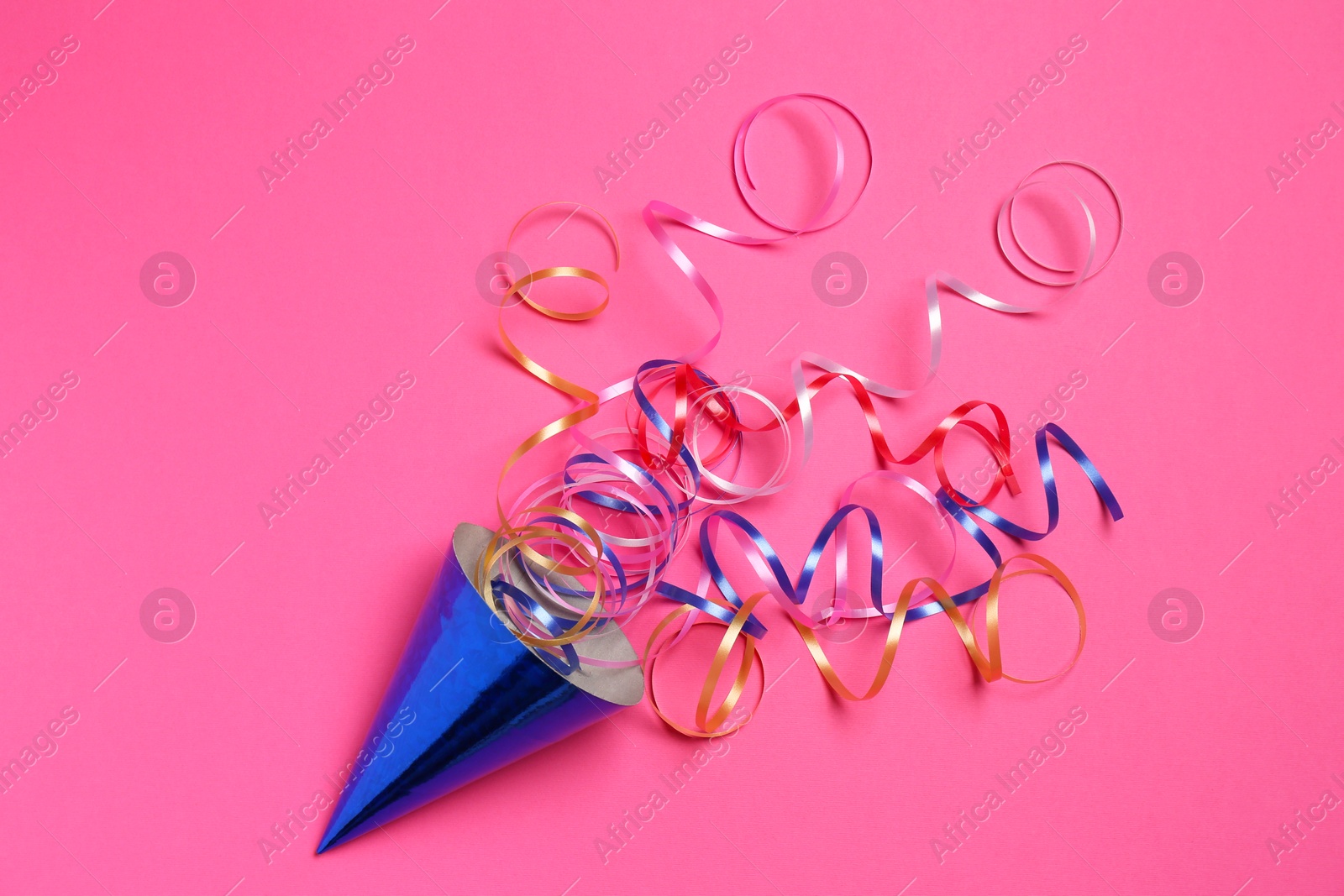 Photo of Blue party hat with streamers on bright pink background, top view