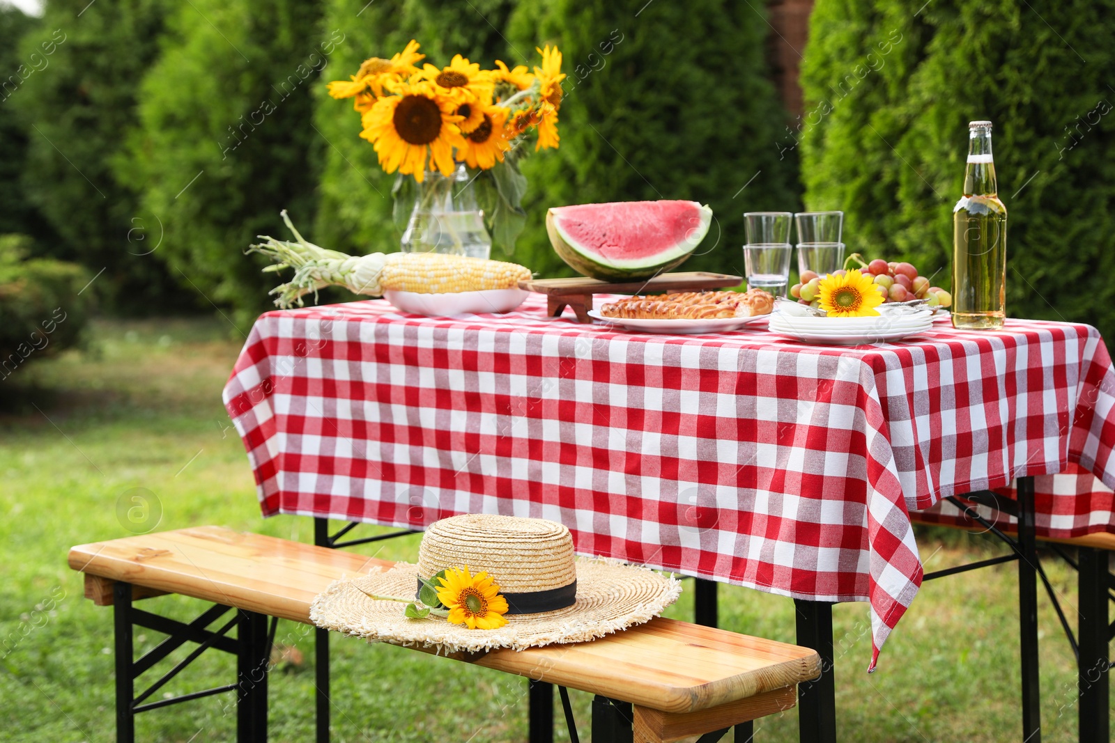 Photo of Fresh fruits, pie, bottle of drink and vase with sunflowers on table in garden