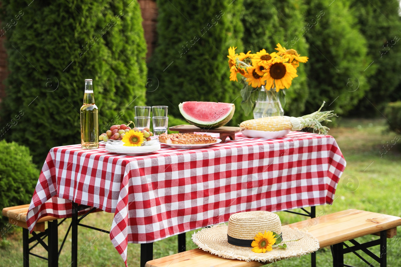 Photo of Fresh fruits, pie, bottle of drink and vase with sunflowers on table in garden