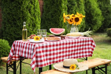 Fresh fruits, pie, bottle of drink and vase with sunflowers on table in garden