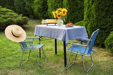 Photo of Vase of sunflowers, corn and grapes on table in garden