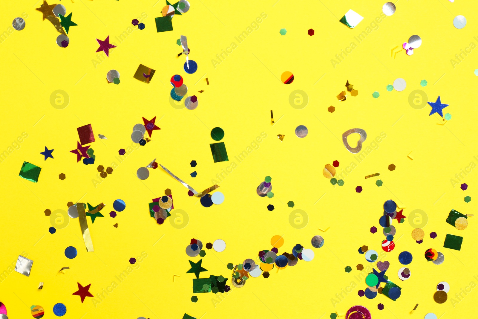 Photo of Shiny confetti on yellow background, top view