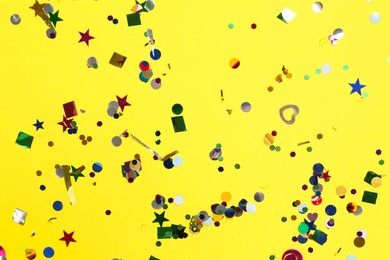 Shiny confetti on yellow background, top view