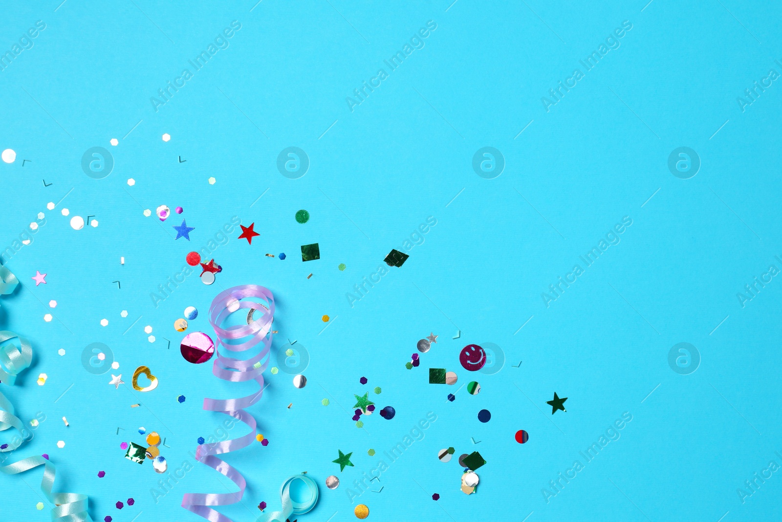 Photo of Shiny confetti and party streamers on light blue background, flat lay. Space for text