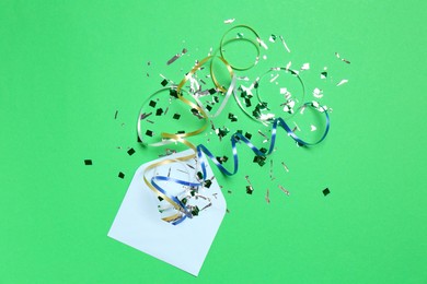 Photo of Shiny confetti and party streamers flying out of envelope on green background, flat lay