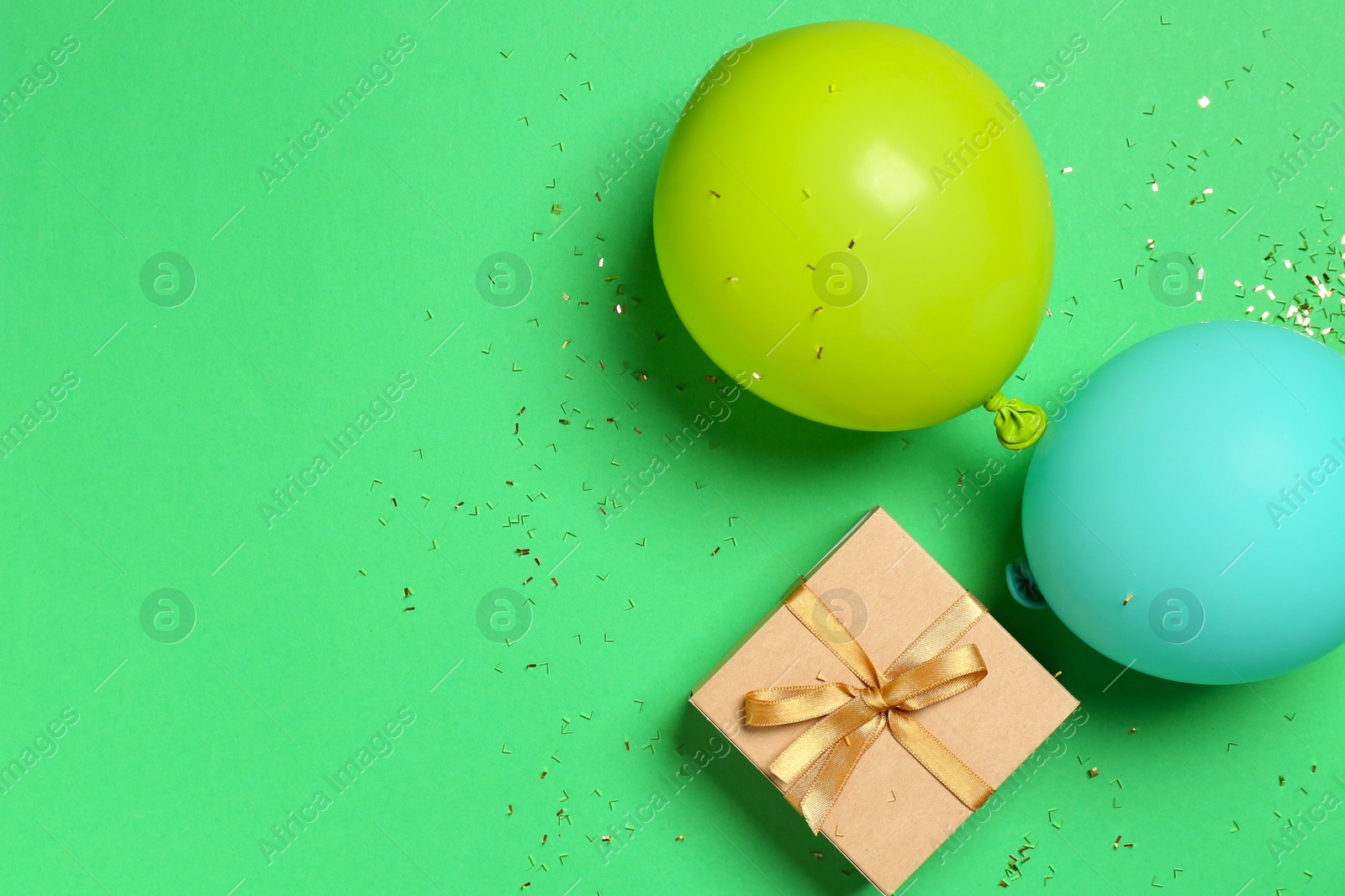 Photo of Gift box, balloons and shiny confetti on green background, flat lay. Space for text