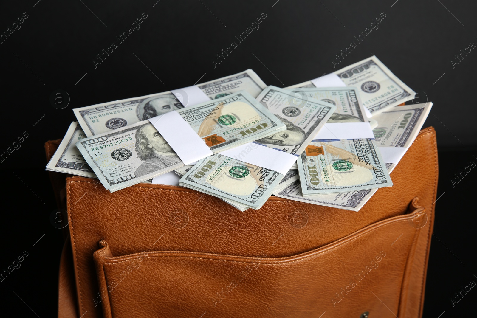 Photo of Dollar banknotes in leather bag on black background, closeup