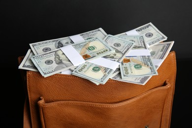 Photo of Dollar banknotes in leather bag on black background, closeup