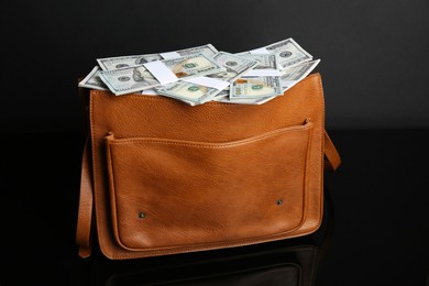 Photo of Dollar banknotes in leather bag on black mirror surface