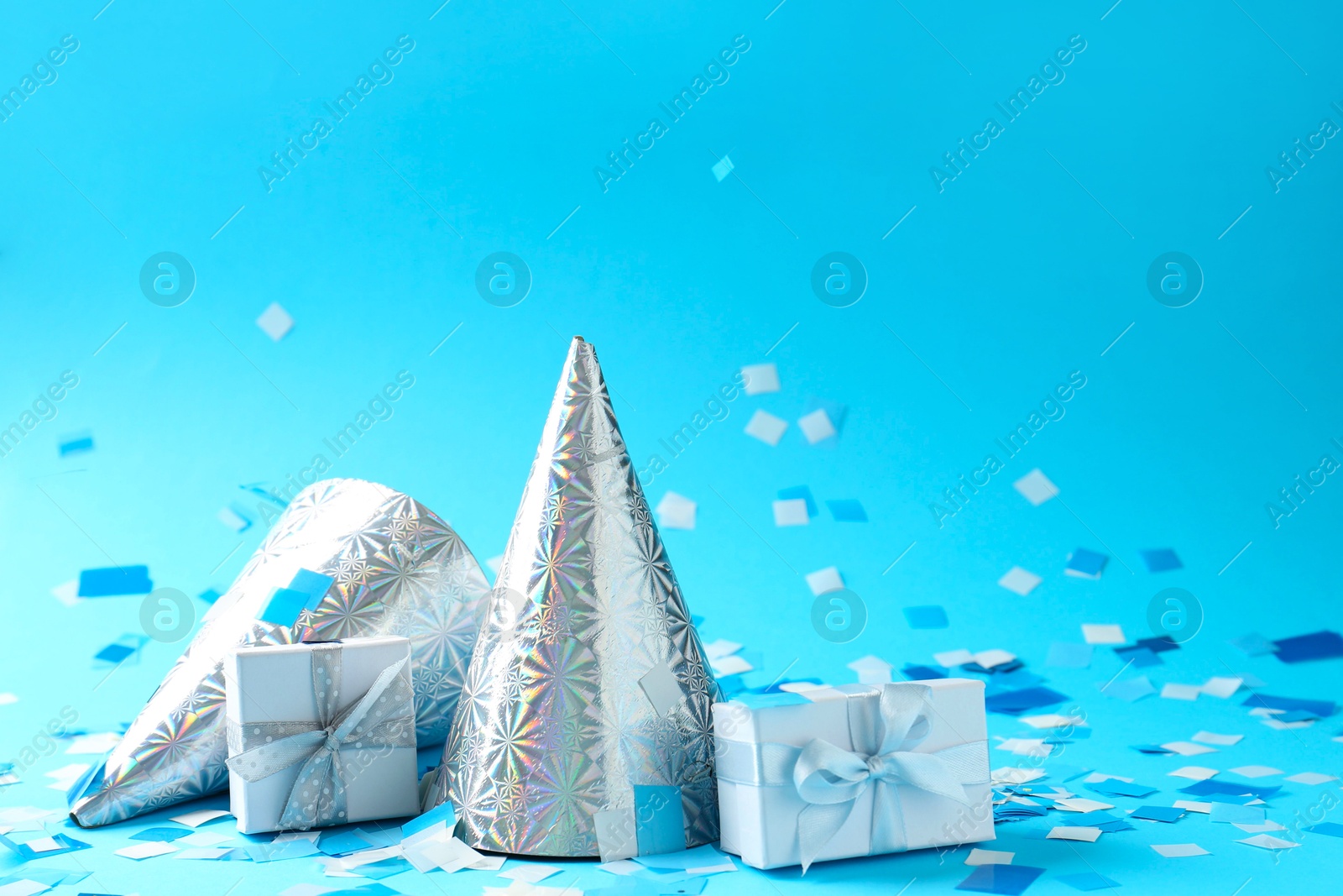 Photo of Beautiful confetti, gift boxes and party hats on light blue background, closeup. Space for text