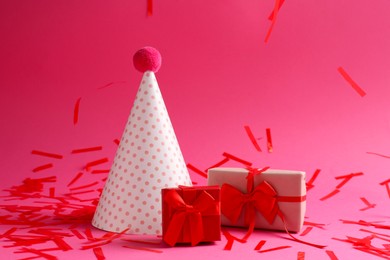 Photo of Beautiful confetti falling on party hat and gift boxes against pink background