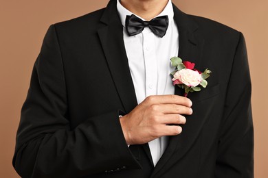 Photo of Groom in suit with stylish boutonniere on beige background, closeup