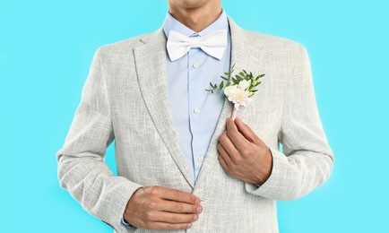 Photo of Groom in suit with stylish boutonniere on light blue background, closeup