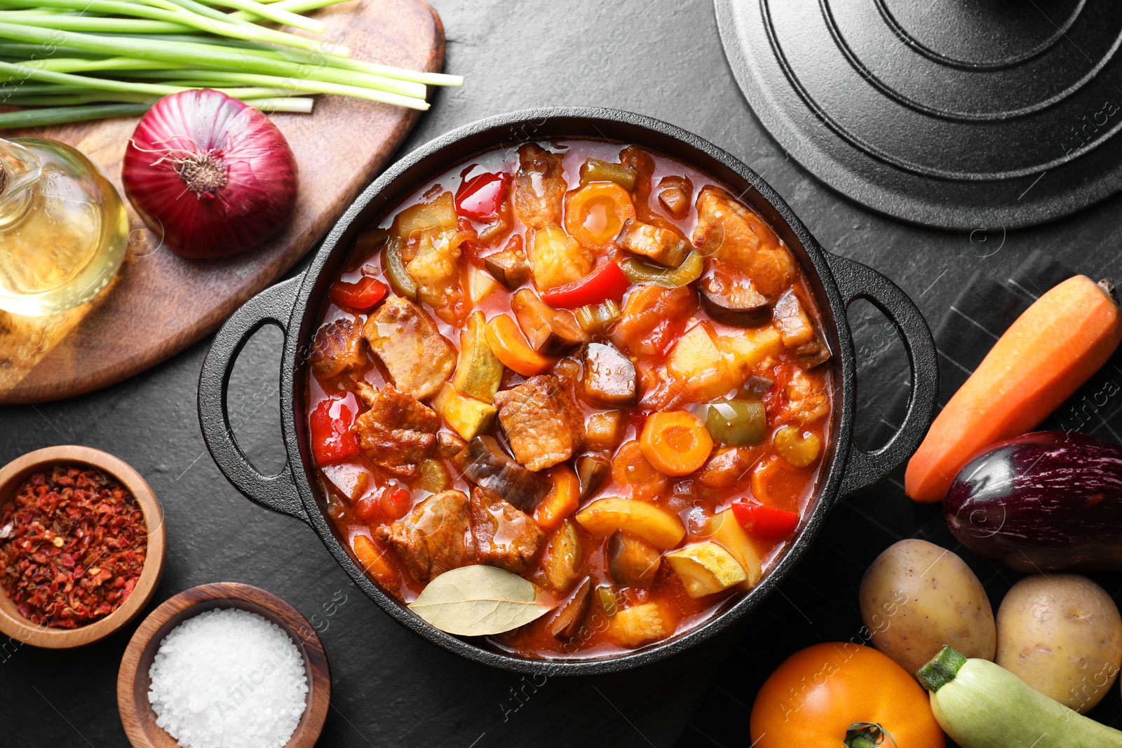 Photo of Delicious stew with vegetables in pot and ingredients on gray textured table, flat lay