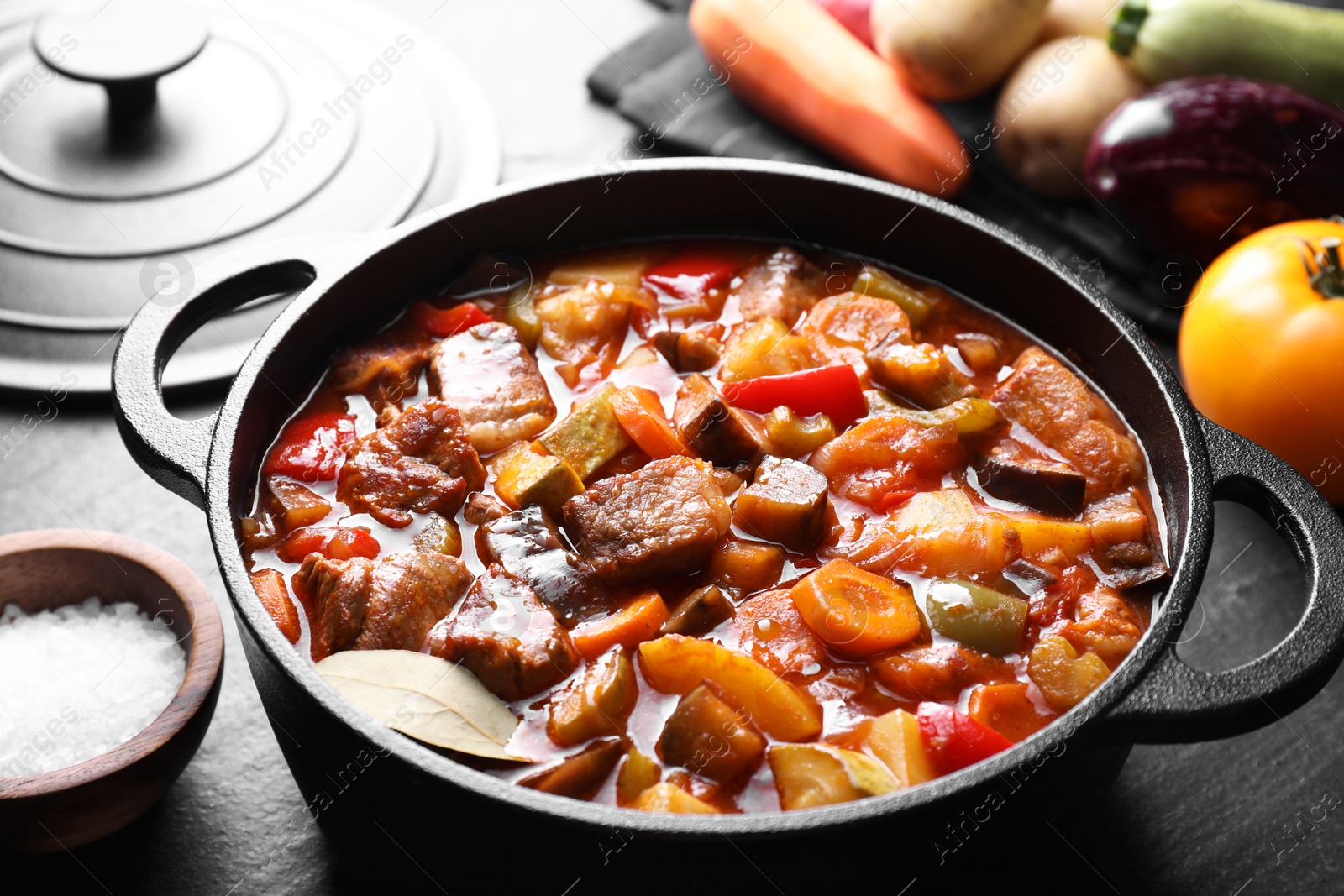 Photo of Delicious stew with vegetables in pot and ingredients on gray textured table, closeup