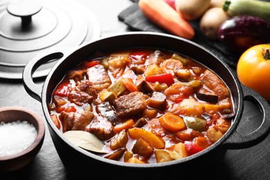 Delicious stew with vegetables in pot and ingredients on gray textured table, closeup