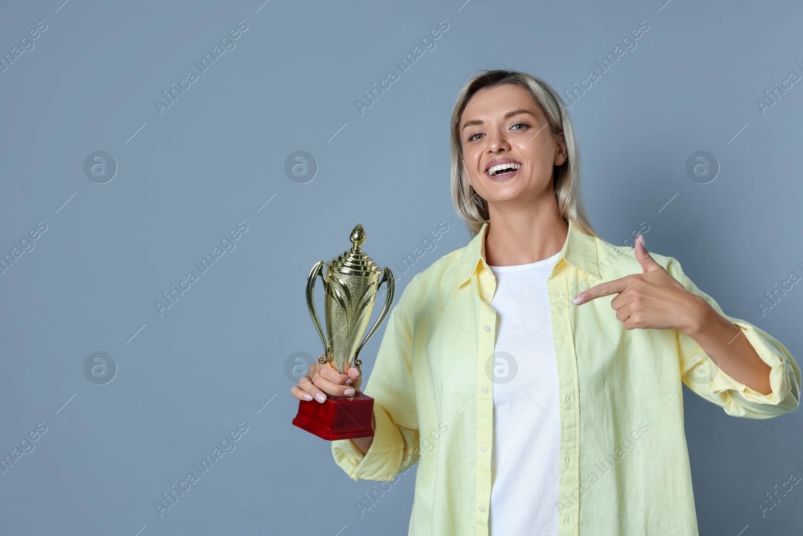 Photo of Happy winner with golden trophy cup on gray background, space for text