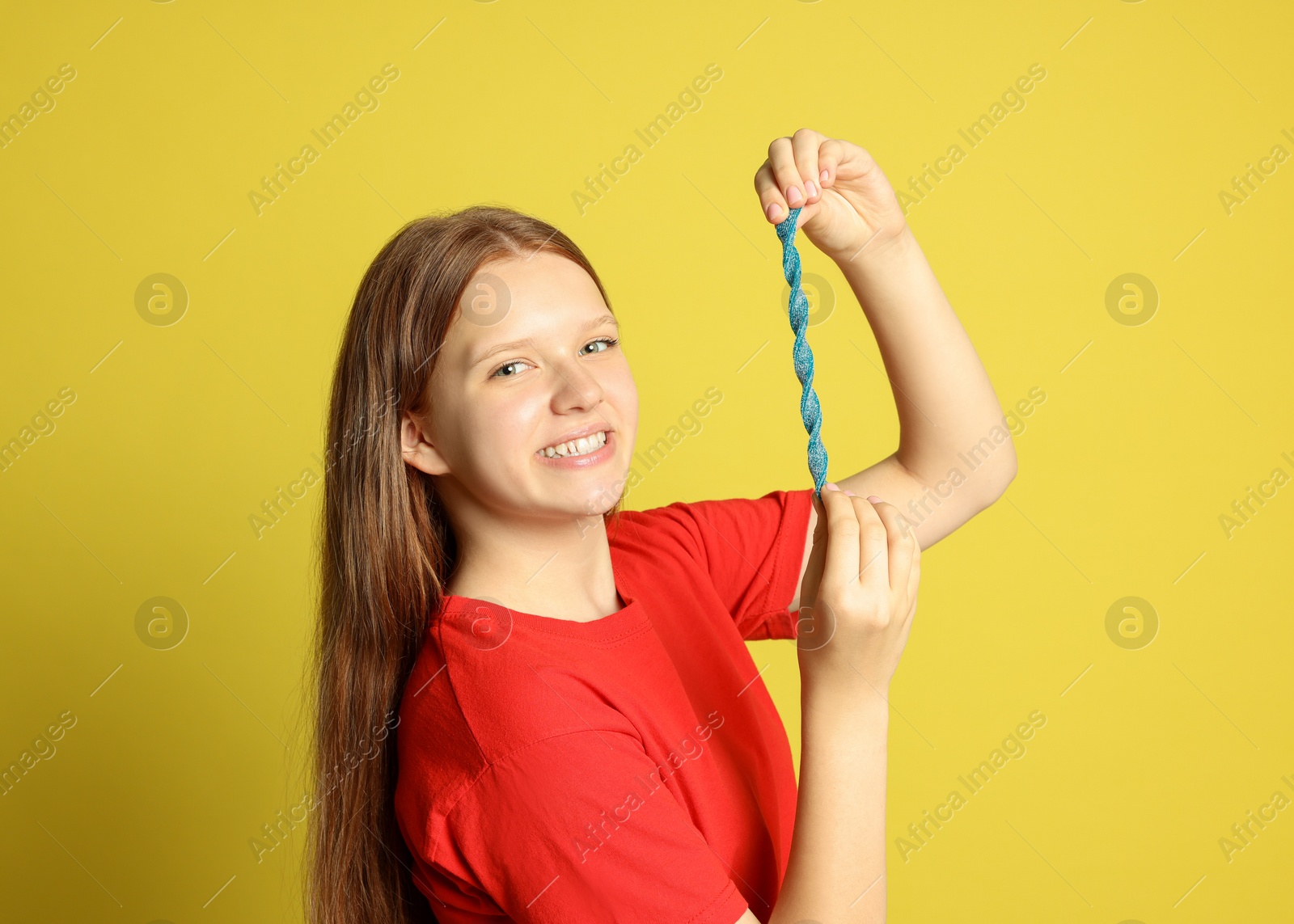 Photo of Happy teenage girl holding tasty gummy candy on yellow background