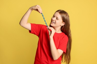 Photo of Happy teenage girl holding tasty gummy candy on yellow background