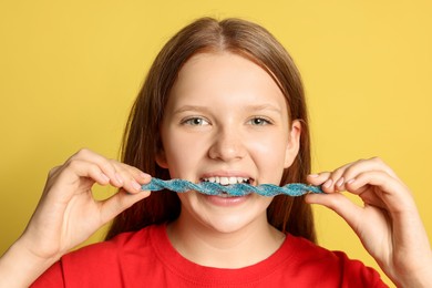 Photo of Teenage girl eating tasty gummy candy on yellow background