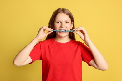 Teenage girl eating tasty gummy candy on yellow background