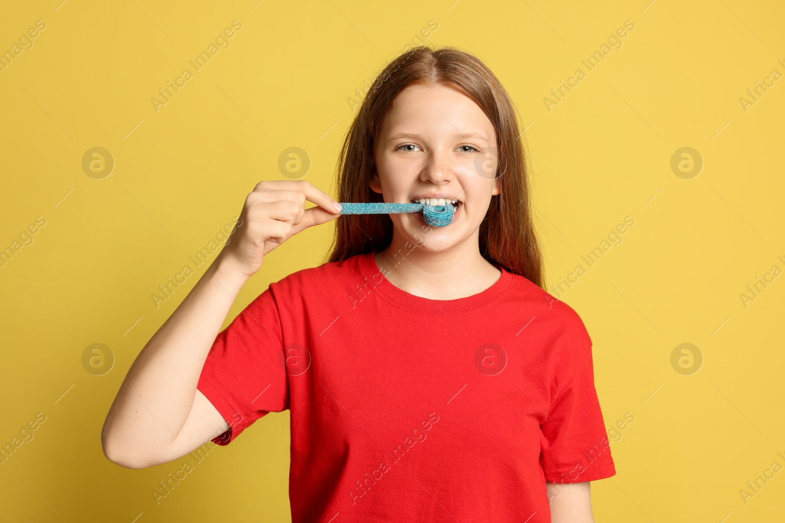 Photo of Teenage girl eating tasty gummy candy on yellow background