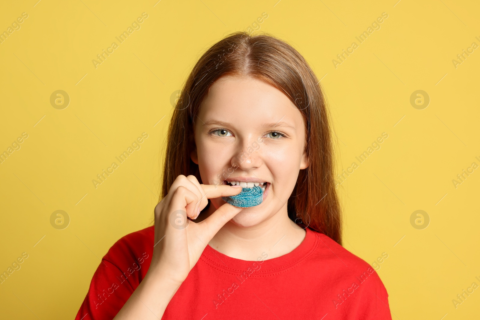 Photo of Teenage girl eating tasty gummy candy on yellow background