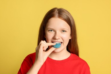 Photo of Teenage girl eating tasty gummy candy on yellow background