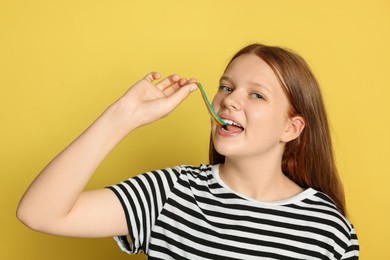 Photo of Teenage girl eating tasty rainbow sour belt on yellow background