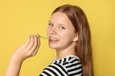 Teenage girl eating tasty rainbow sour belt on yellow background