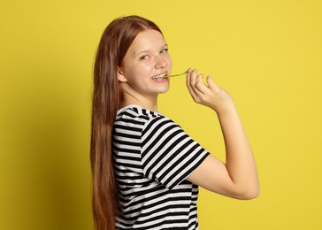 Photo of Teenage girl eating tasty rainbow sour belt on yellow background