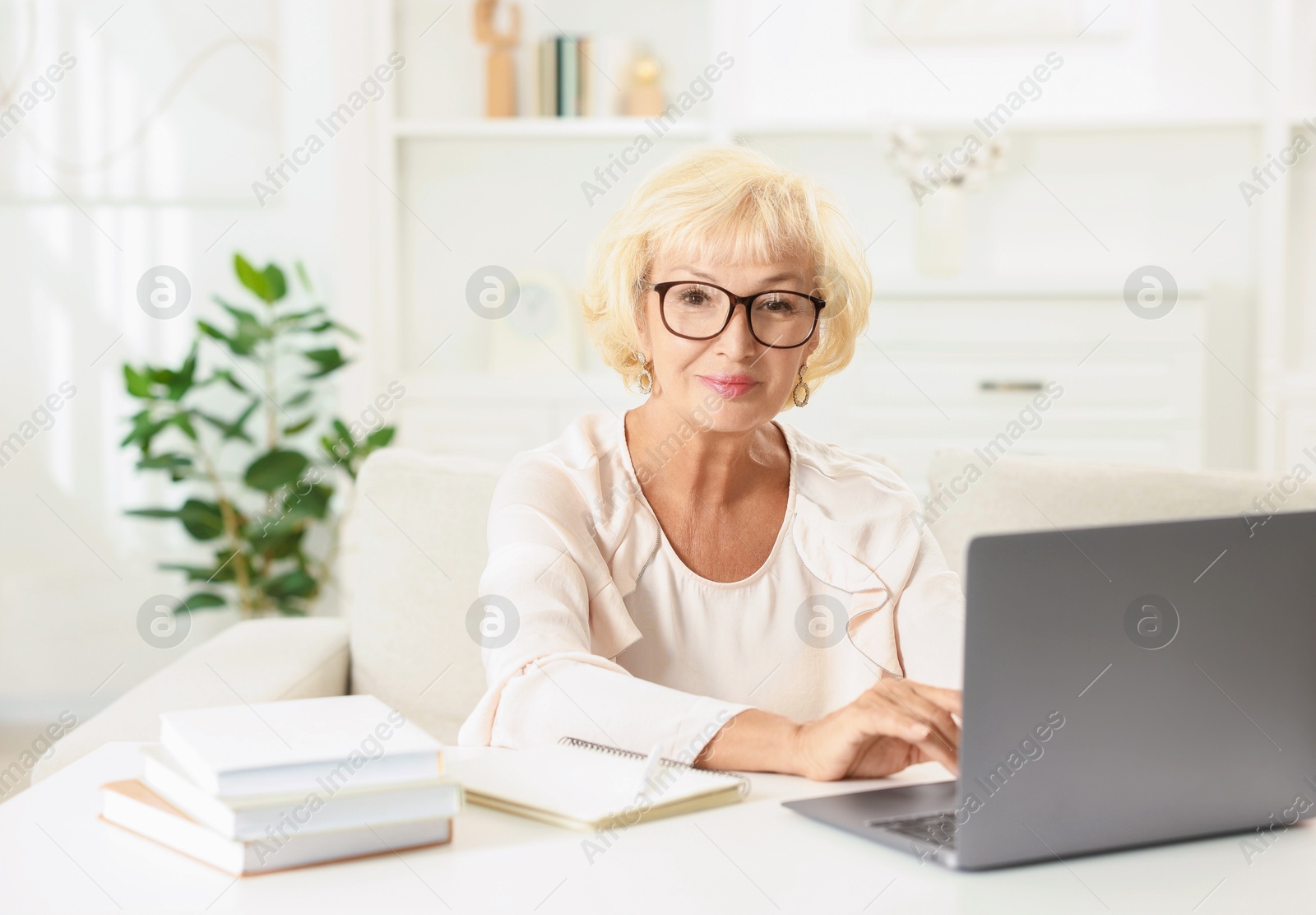 Photo of Beautiful senior woman using laptop at white table indoors