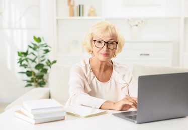 Photo of Beautiful senior woman using laptop at white table indoors