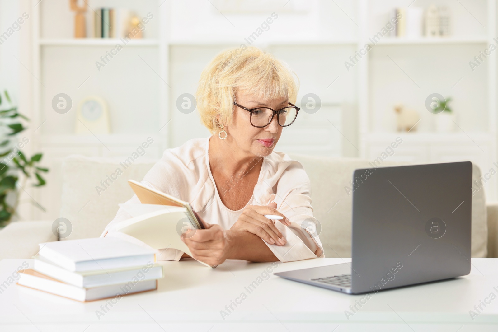 Photo of Beautiful senior woman using laptop at white table indoors