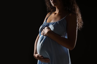 Pregnant woman on black background, closeup view