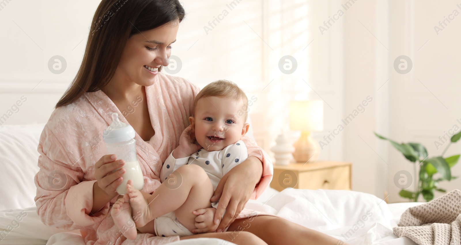 Photo of Mother holding cute little baby and bottle of milk on bed at home. Space for text