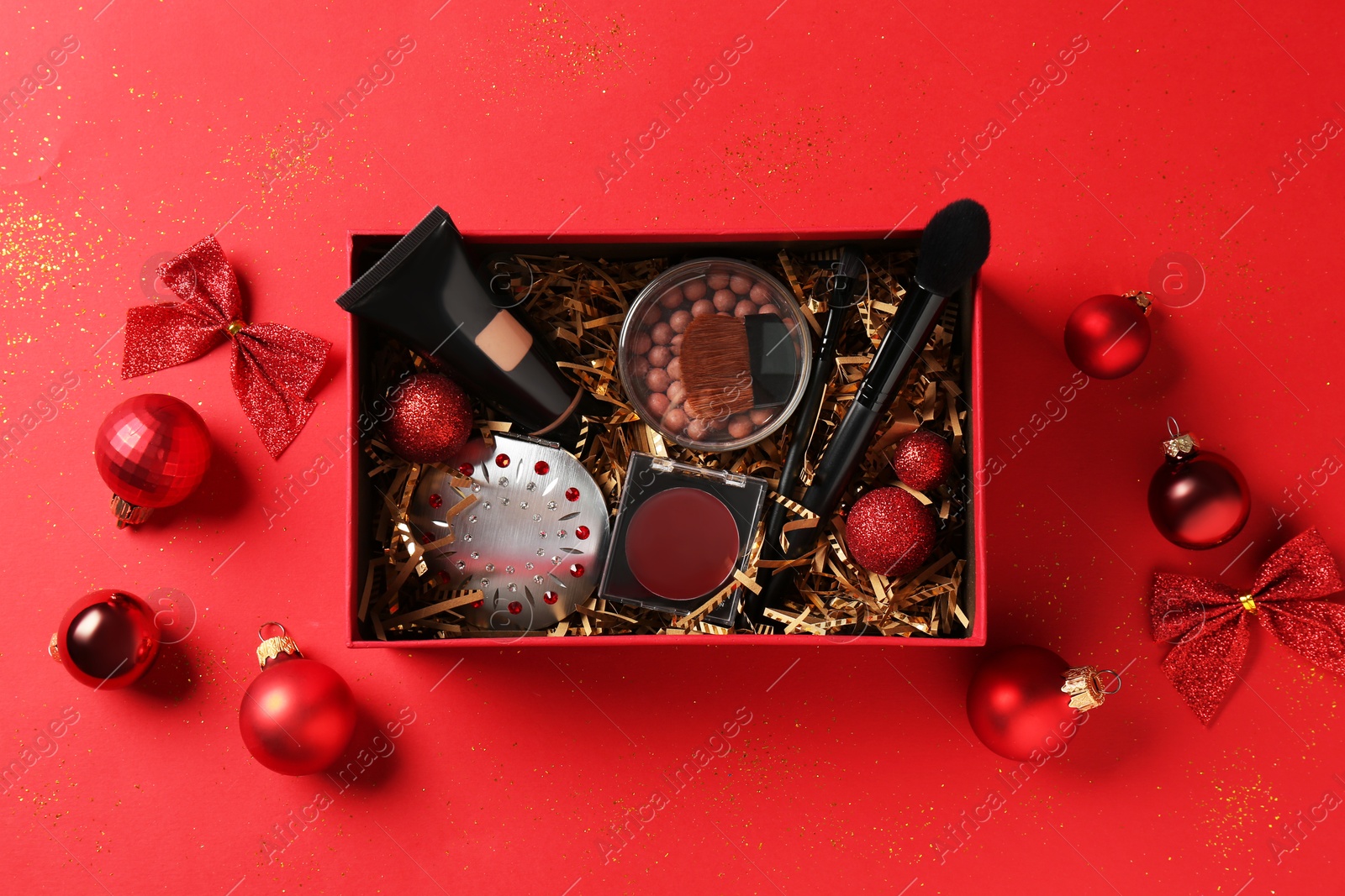 Photo of Christmas gift box with cosmetic products and festive decor on red background, top view