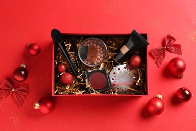 Christmas gift box with cosmetic products and festive decor on red background, top view