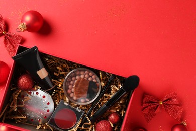 Christmas gift box with cosmetic products and festive decor on red background, top view. Space for text