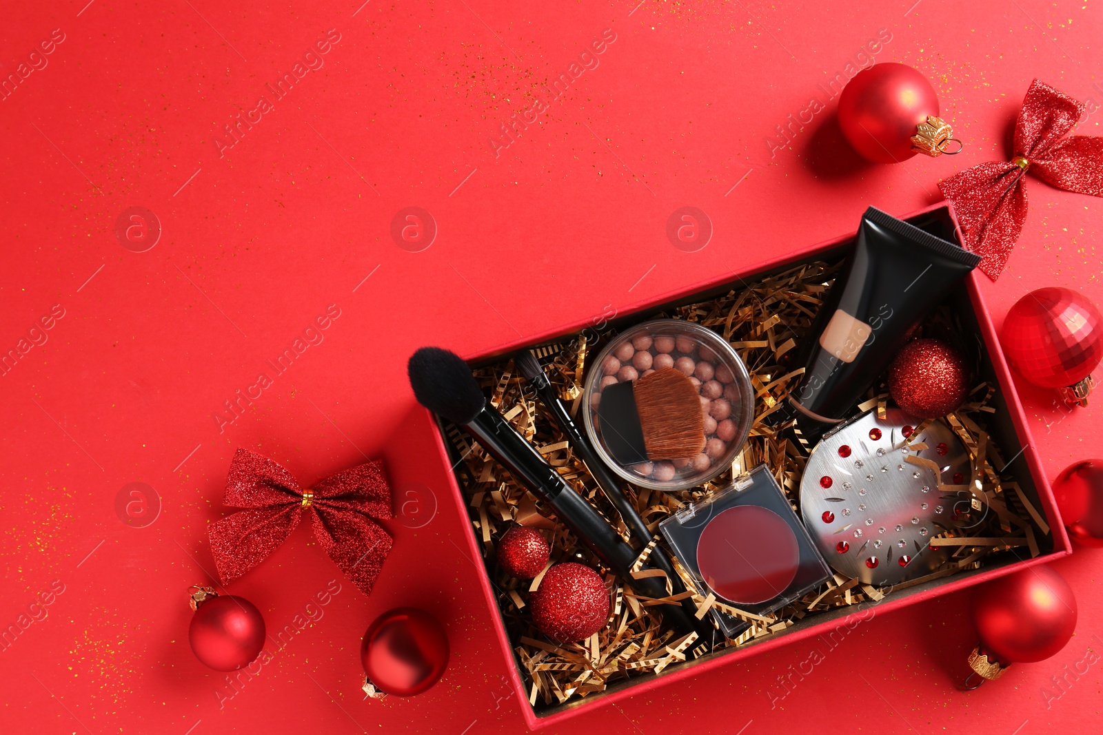 Photo of Christmas gift box with cosmetic products and festive decor on red background, top view. Space for text