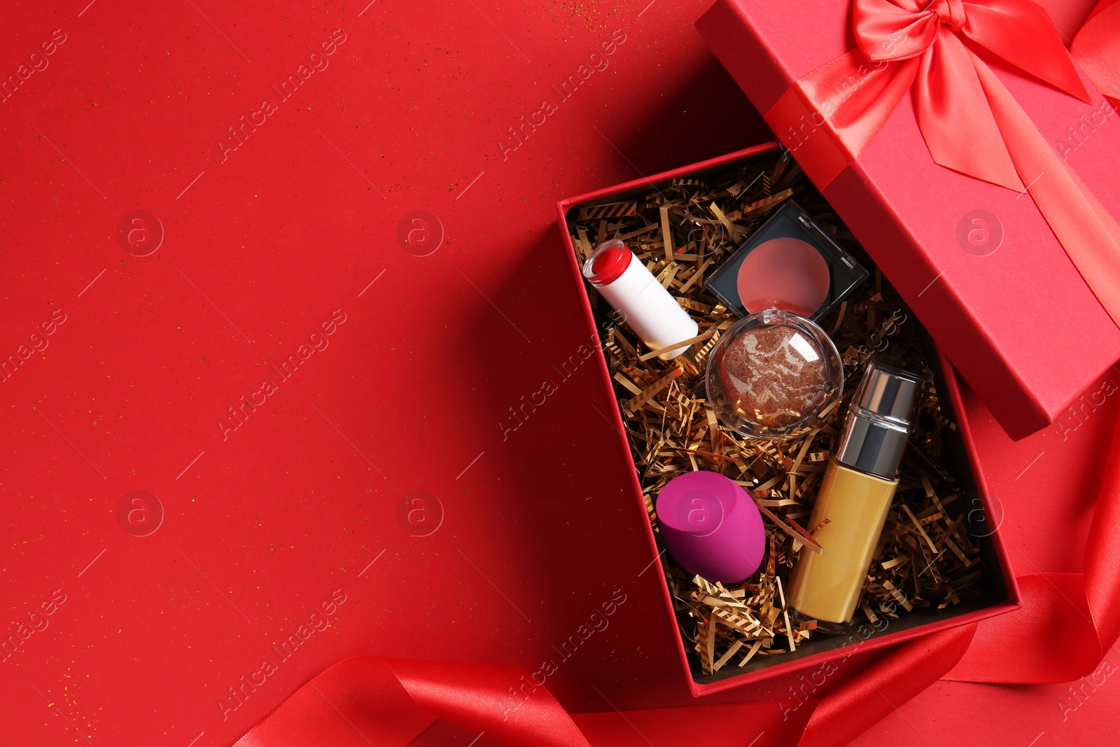 Photo of Christmas gift box with cosmetic products on red background, top view. Space for text